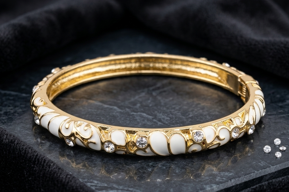 A gold-plated bangle bracelet decorated with white mother-of-pearl inlays and small clear rhinestones, displayed on a black textured surface with a black velvet cloth background. A brand logo for 'Pristyn Jewels' is visible in the bottom right corner.