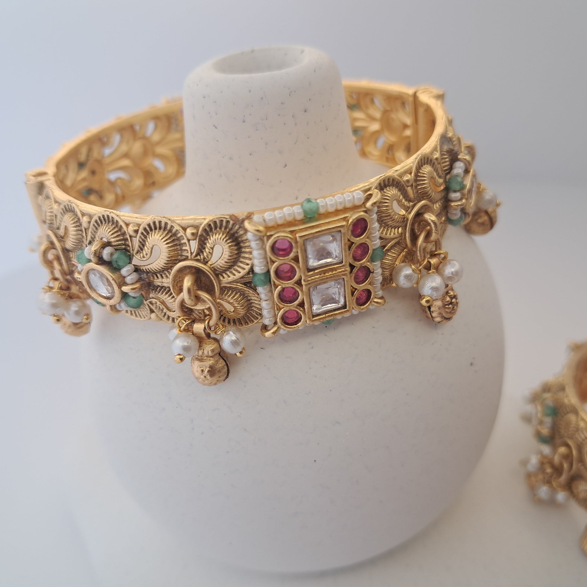 Ornate gold necklace with gemstones on a white stand