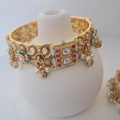 Ornate gold necklace with gemstones on a white stand