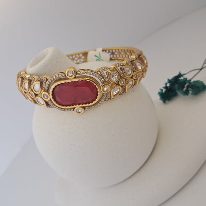 Gold bracelet with a red stone on a white stand with a blurred background