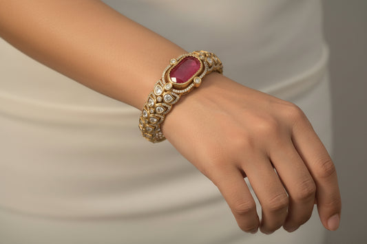 Gold bracelet with a red gemstone on a wrist against a neutral background