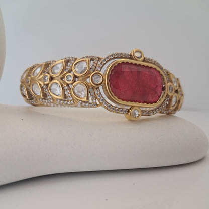Gold bracelet with a red gemstone on a mannequin arm against a white background