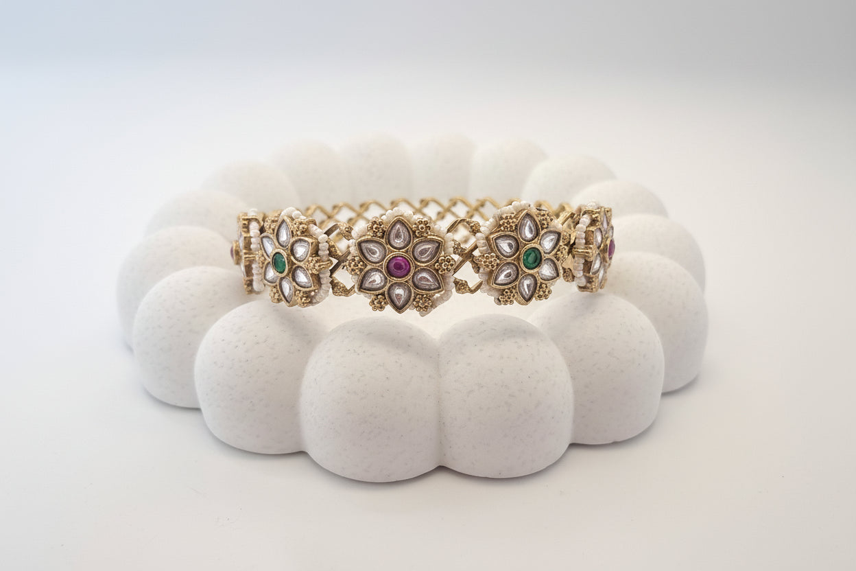 Two gold bracelets with gemstones on a white cushion against a light gray background