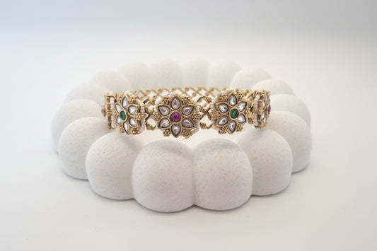 Two gold bracelets with gemstones on a white cushion against a light gray background
