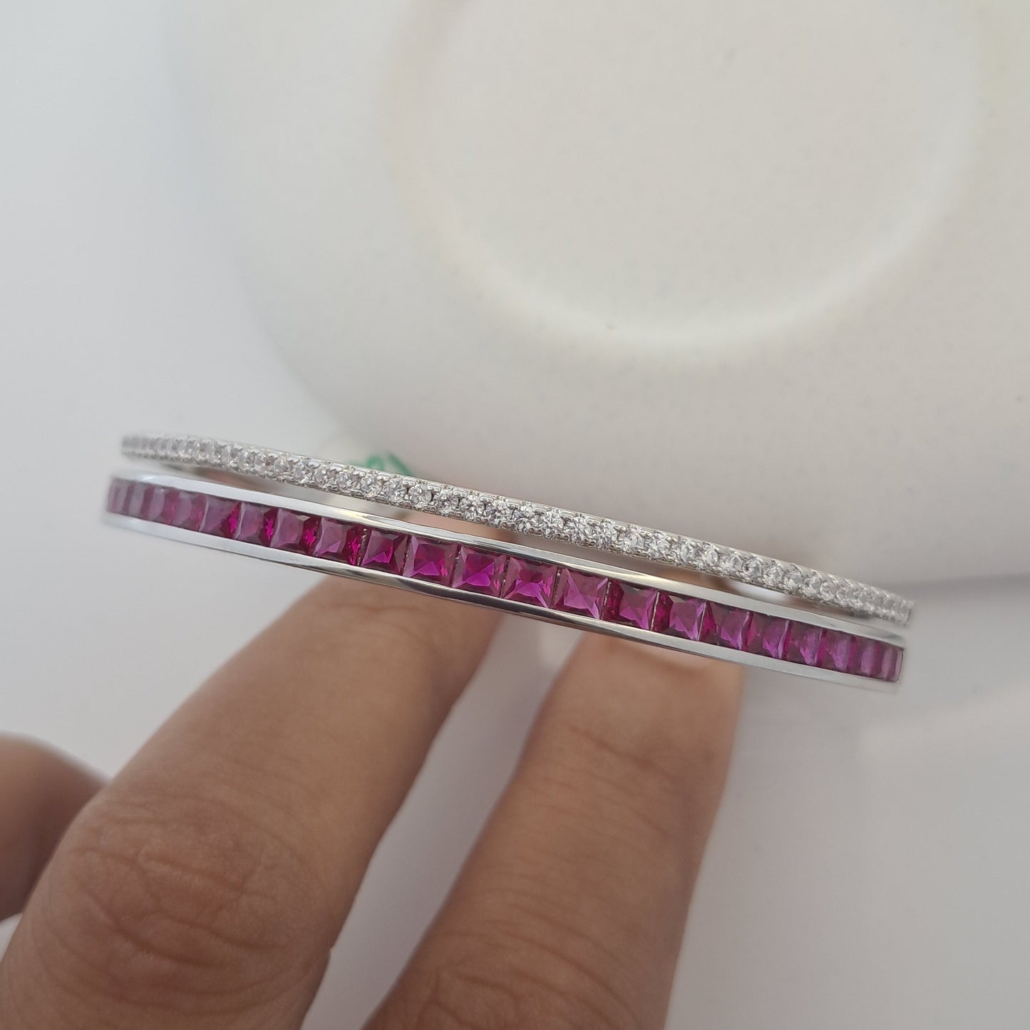 Close-up of a hand holding a bracelet with red gemstones on a white background