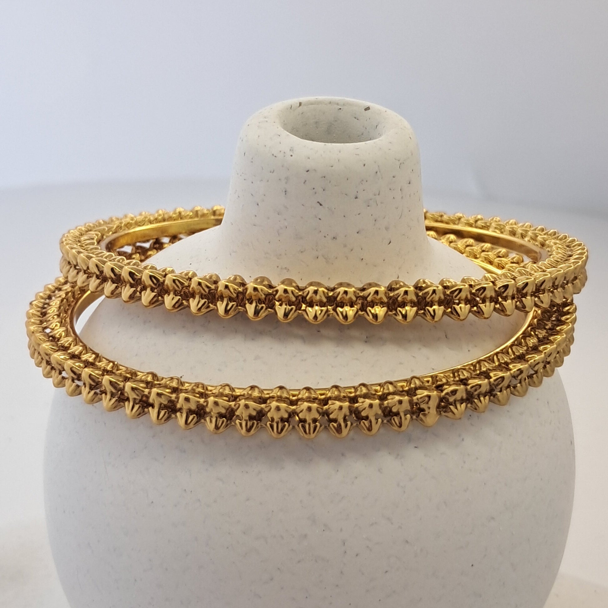 Gold bracelet on a white cylindrical stand with a plain background