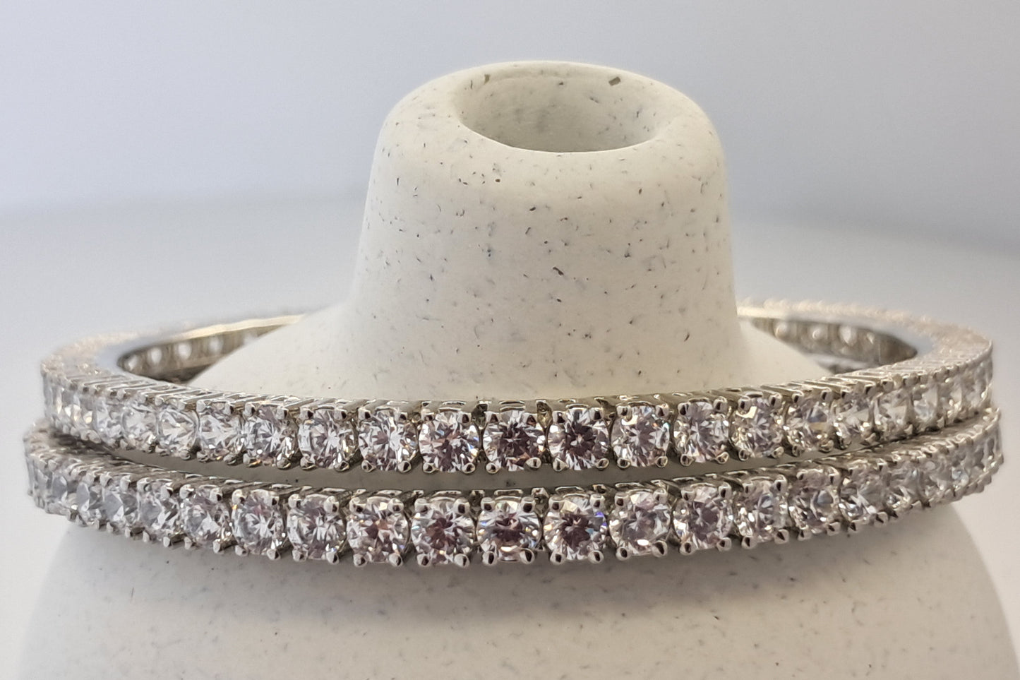 Two diamond bangles on a white stone stand against a light gray background