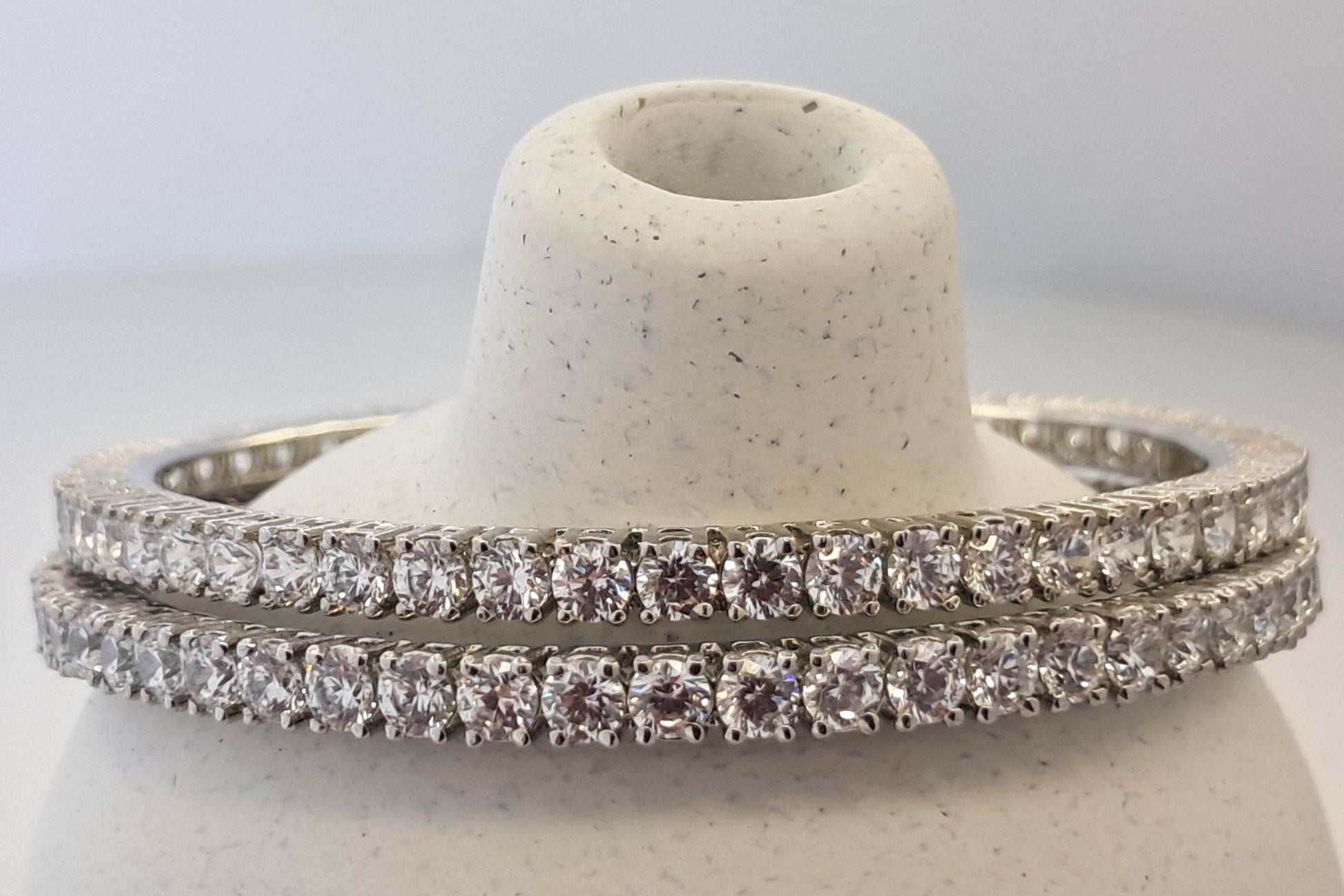 Two diamond bangles on a white stone stand against a light gray background