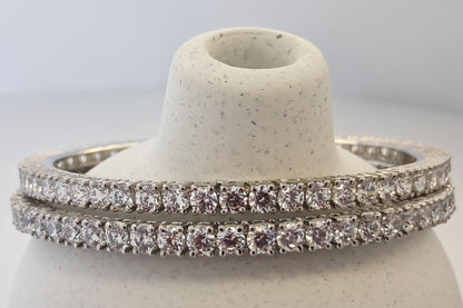 Two diamond bangles on a white stone stand against a light gray background