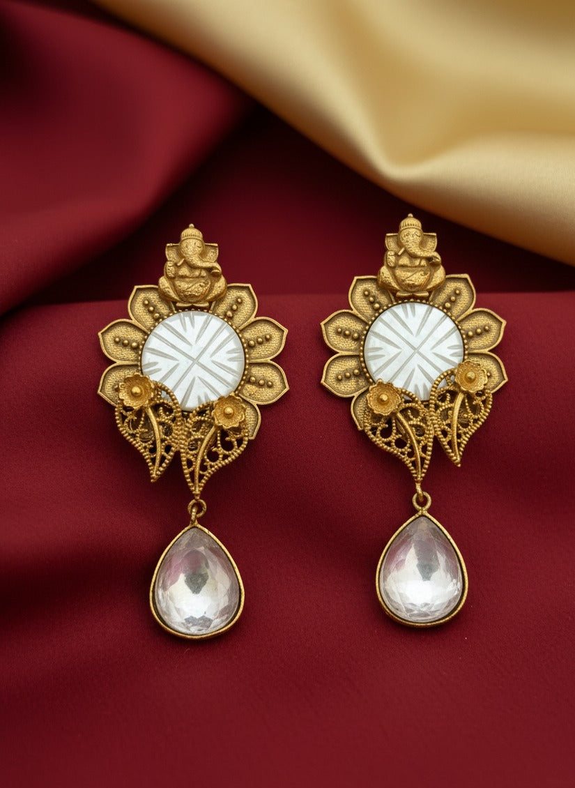 Ornate gold earrings with white stones on a red fabric background