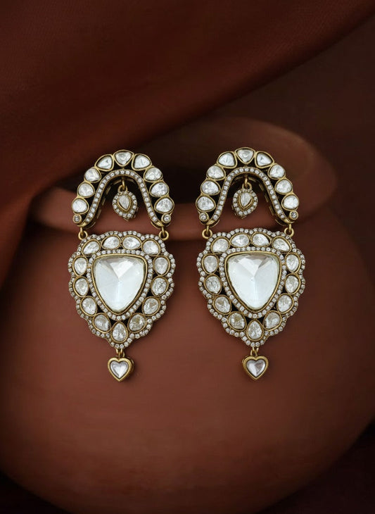 Pair of ornate earrings with heart-shaped designs on a brown fabric background