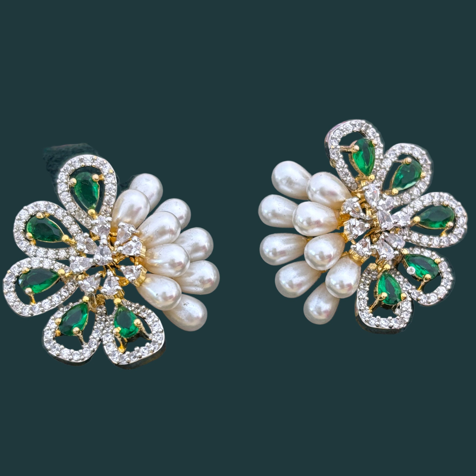 Pair of decorative earrings with pearls and gemstones on a dark green fabric background.