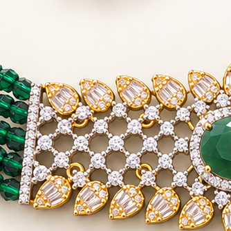 A gold and green gemstone jewelry set featuring a multi-strand beaded necklace with a central floral design, matching drop earrings, and clear accent stones, displayed on a light cream background.