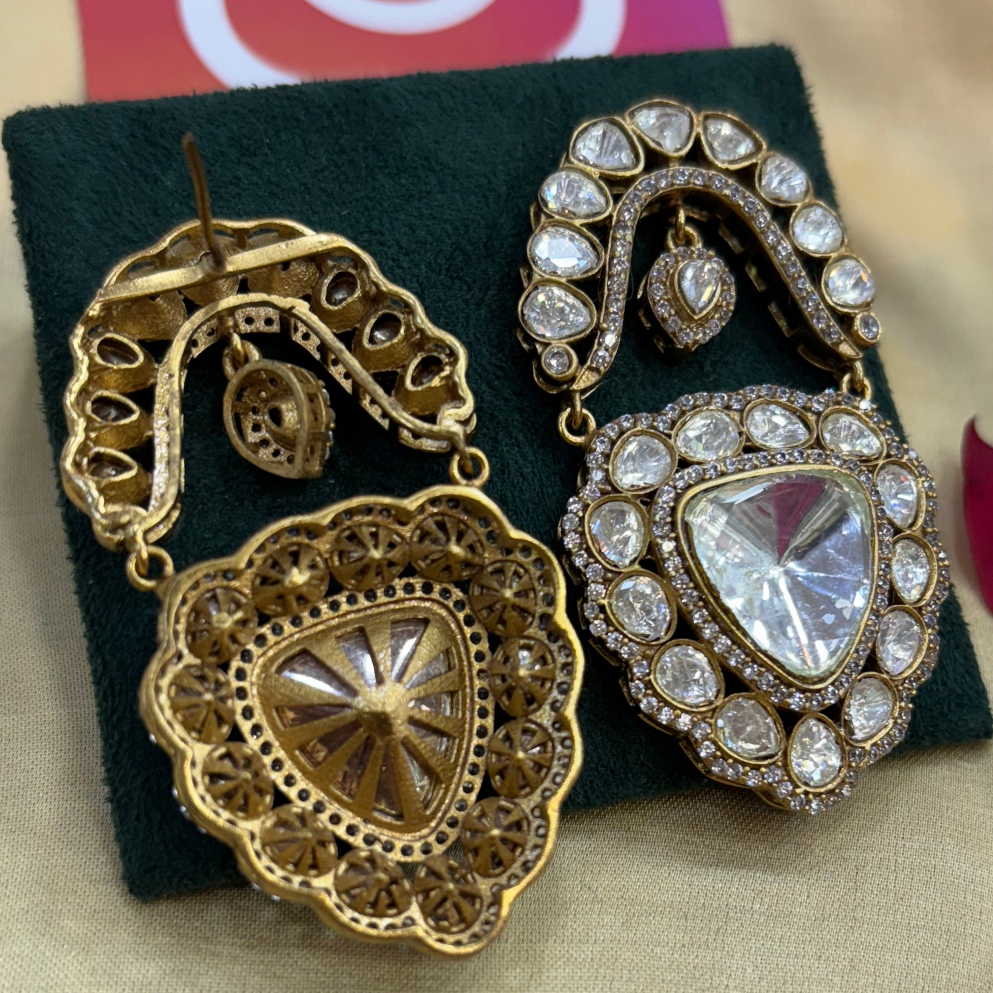 Gold and crystal earrings on a green cushion with a blurred background
