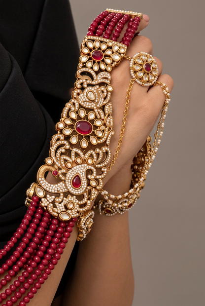 A woman wearing a black evening gown and ornate gold and red jewelry, including a statement necklace draped over her shoulders and matching earrings, posed against a neutral gray studio background.