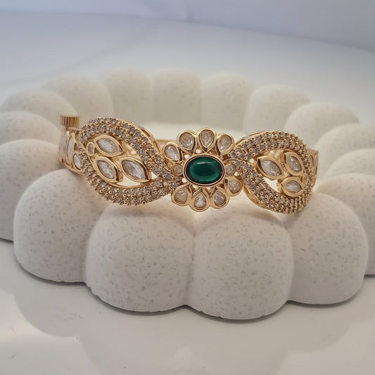 Gold bracelet with green gemstone on a white textured stand
