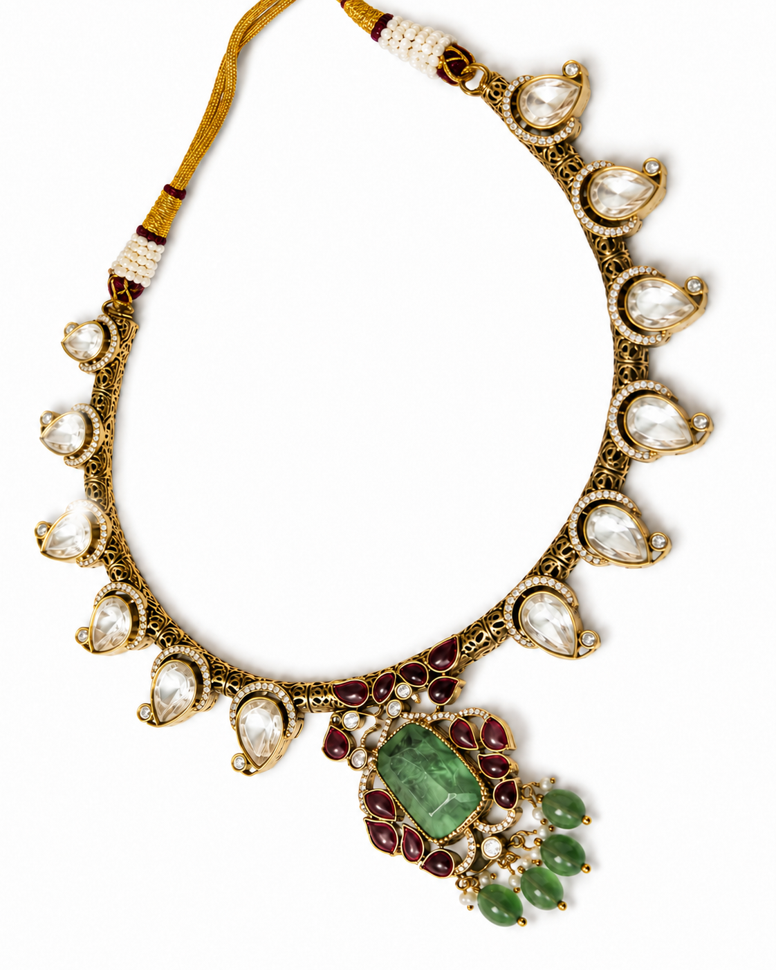An ornate traditional Indian gold-plated necklace (Kara) featuring a large central green stone, red gemstone accents, green bead drops, and clear teardrop-shaped stones along the border.