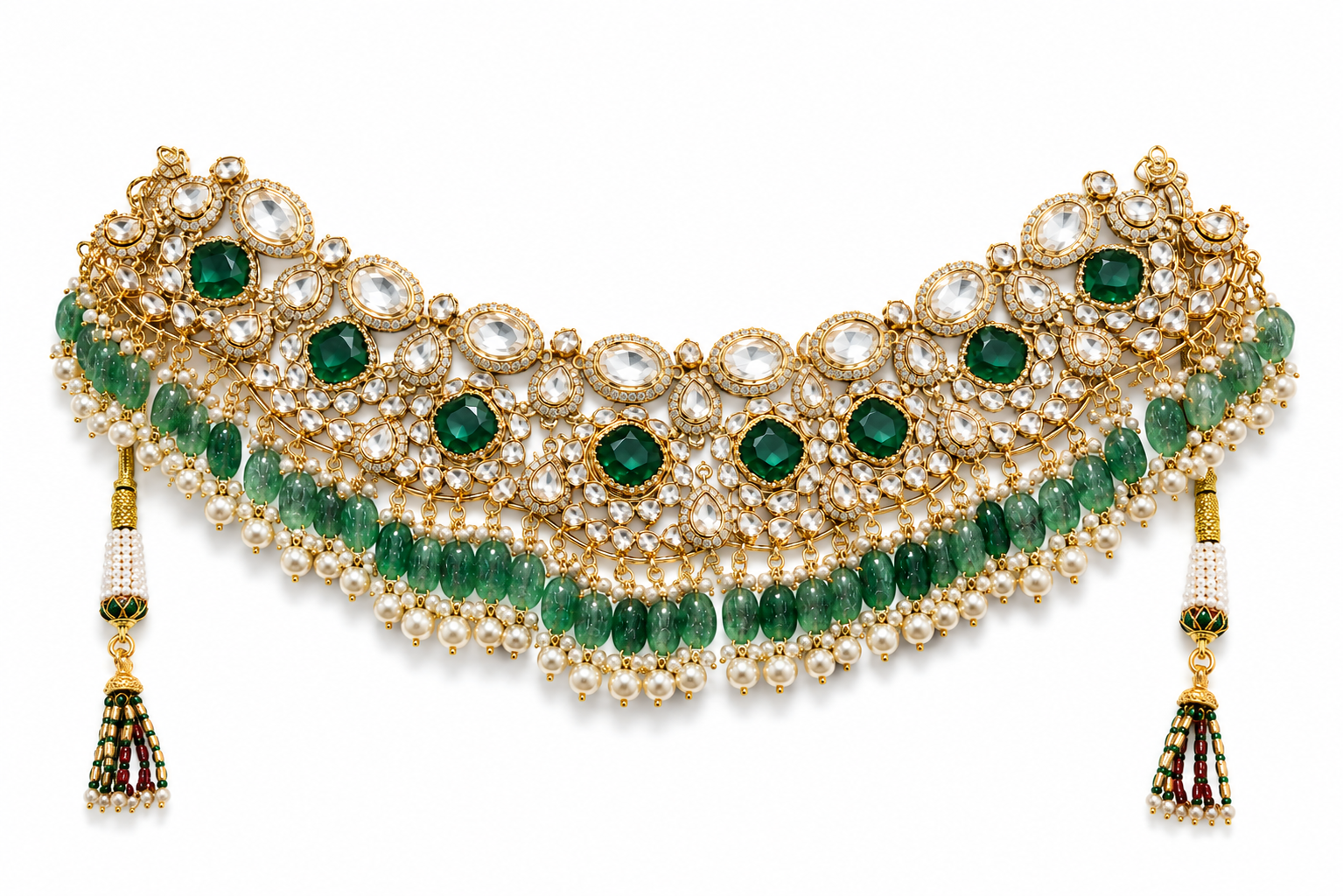 An ornate gold-toned traditional necklace with green emerald-cut stones, white pearl-like beads, and dangling tassel earrings, shown on a plain white background.