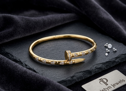 A gold-toned hinged cuff bracelet with pavé-set Cubic Zircon Triple "A" Quality, displayed on a dark textured surface with branded card and small loose stones nearby. The visible brand on the card is Prism Jewels.