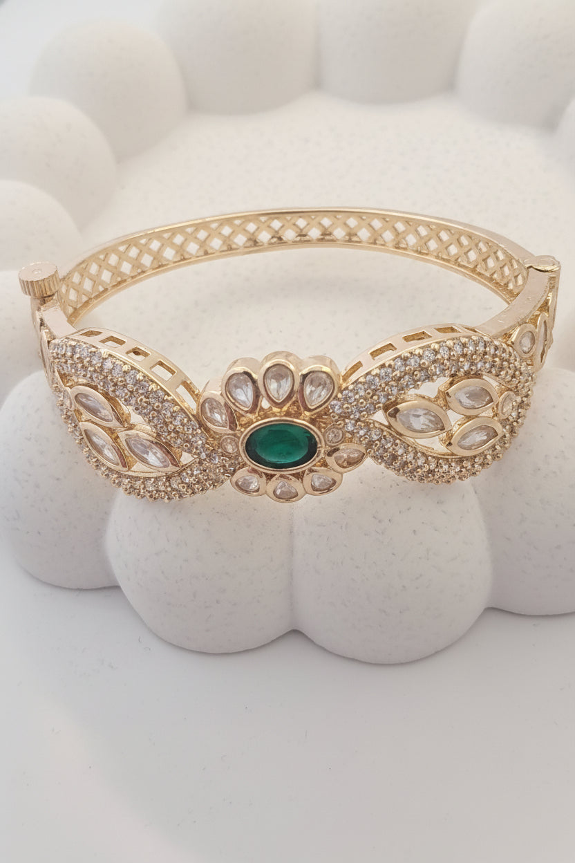Gold bracelet with green gemstone on a white cushion, brand tag visible.