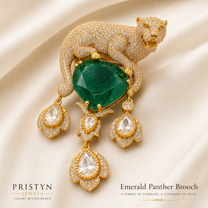An elegant gold panther brooch adorned with pavé-set Cubic Zircon Triple "A" Quality and a large faceted green emerald at its chest, displayed on a draped cream satin fabric. The brooch features three dangling emerald-cut Cubic Zircon Triple "A" Quality drops.
