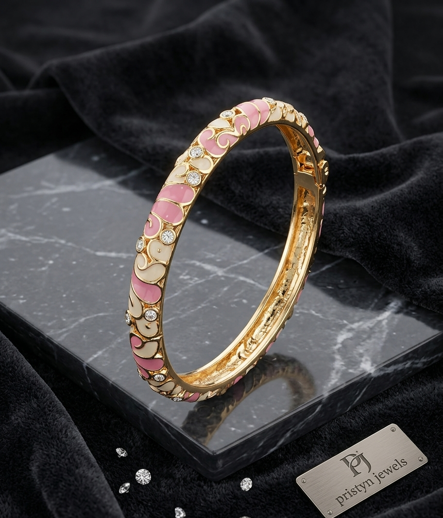 A gold-plated bangle bracelet with pink and cream enamel floral patterns and small clear stones, displayed on a black marble block with black velvet fabric. A brand tag for 'Pristyn Jewels' is visible.