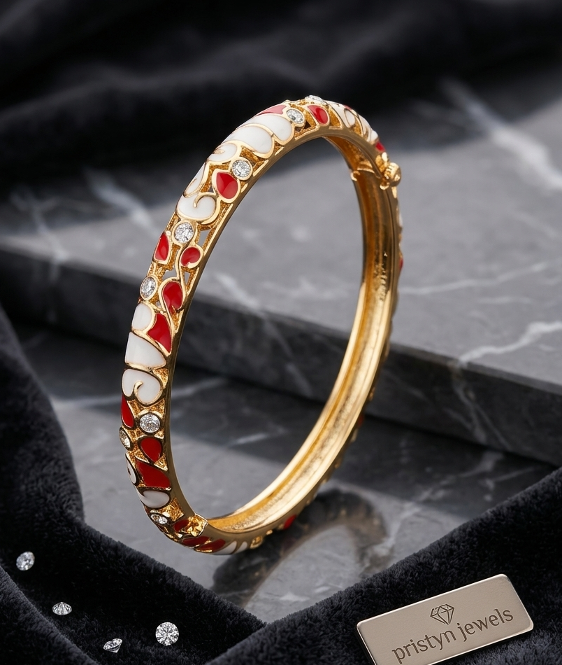 A gold-plated hinged bangle bracelet decorated with white enamel, red enamel, and small clear stones, displayed on a black velvet surface next to a brand tag reading 'pristyn jewels'.