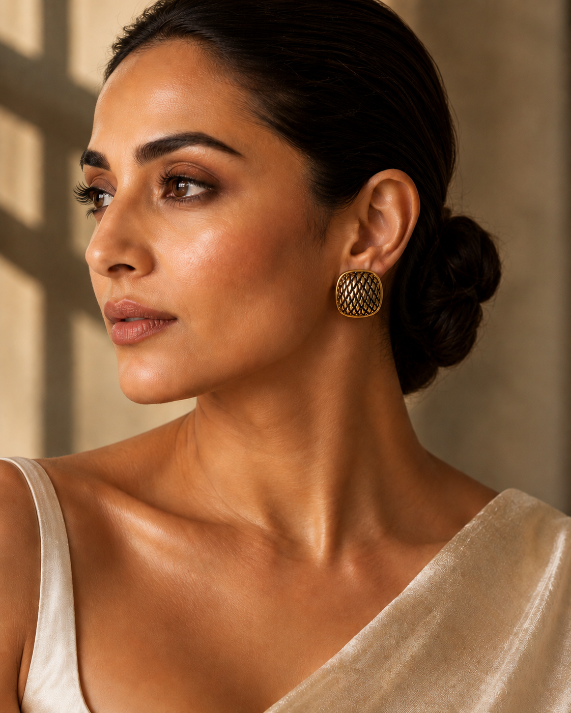 Woman wearing textured gold statement stud earrings with a vibrant floral satin shirt in a luxury editorial portrait.