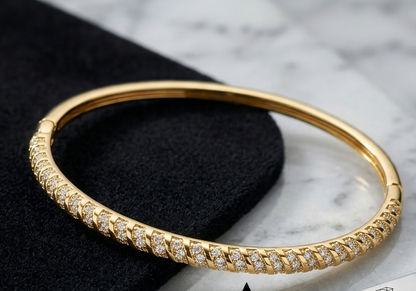 A gold bangle bracelet with a row of small Cubic Zircon Triple "A" Quality, displayed on a black velvet surface over a white marble background. A small brand tag reading CÉDALUME is visible, along with an inset close-up of the bracelet band and an arrow pointing to the product.