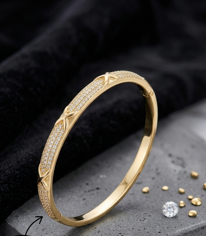 A gold bangle bracelet with pavé-set Cubic Zircon Triple "A" Quality and an X-shaped decorative motif, displayed on a gray stone block with a black velvet cloth. A circular inset shows a close-up of the bracelet band, and a Gemlume brand tag is visible on the surface.